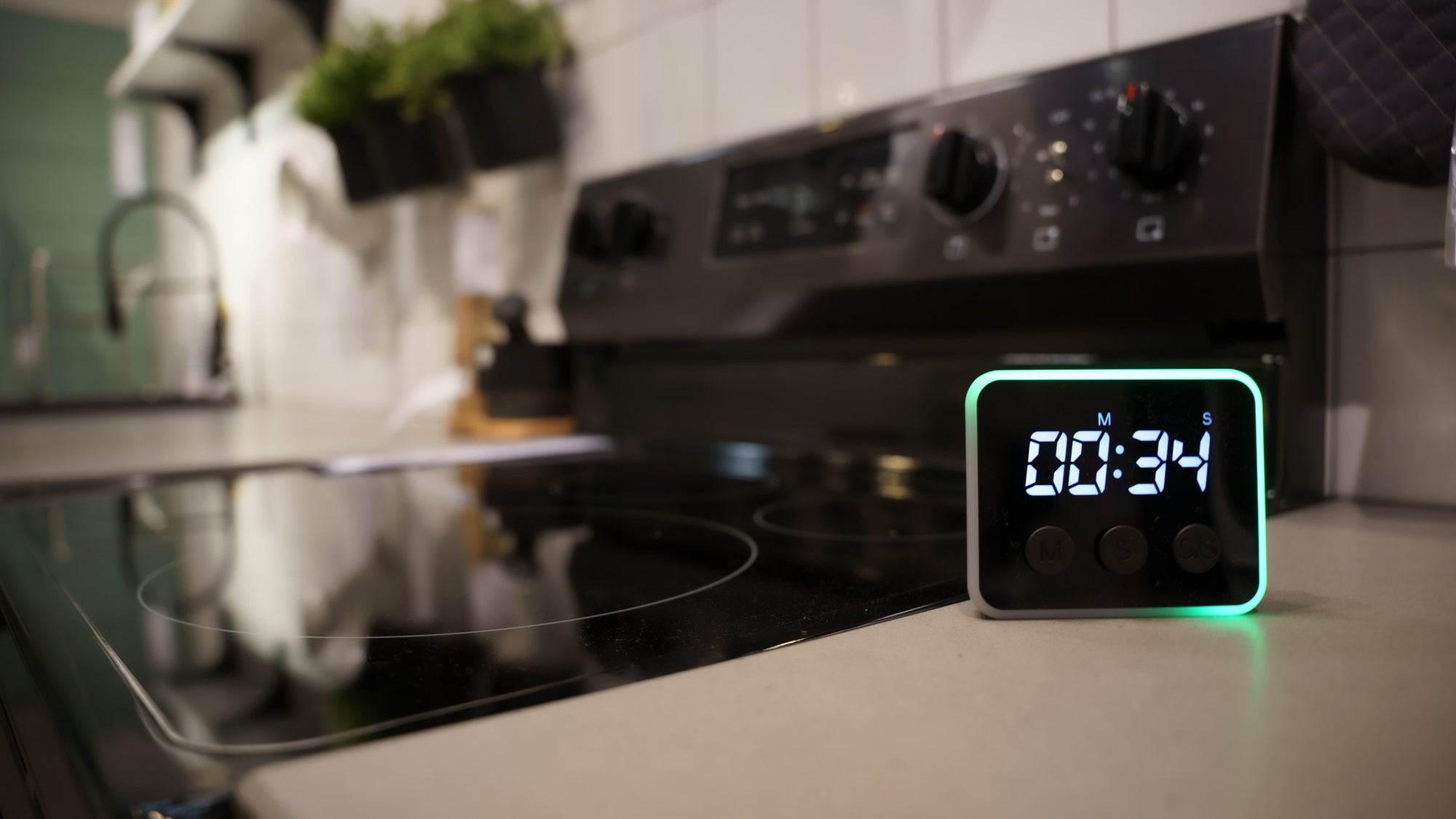 Looptimer visual timer showing 00:34 with green LED light band on a kitchen counter, dark stove behind