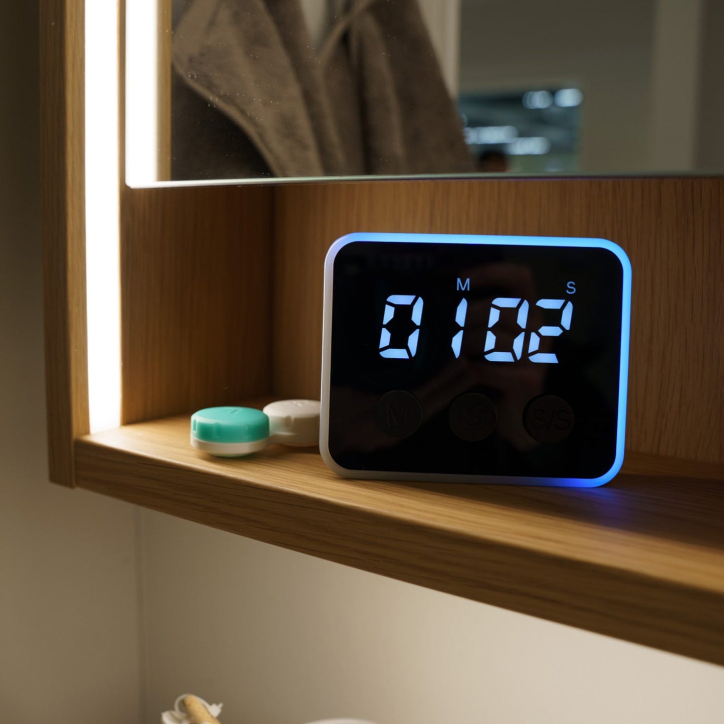 Looptimer visual timer with blue LED light on a wooden bathroom shelf next to a contact lens case