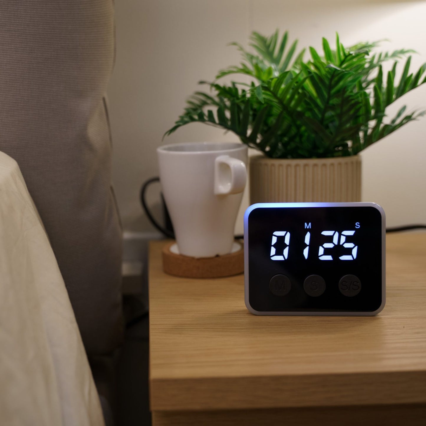 Looptimer visual timer counting down 1 minute 25 seconds on a wooden nightstand beside a plant and mug